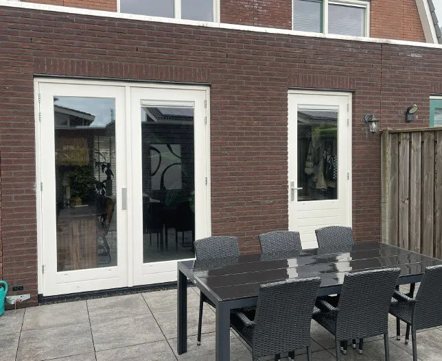 Nieuwe witte openslaande deuren en enkele deur in bakstenen gevel.